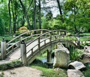 Een houten boogbrug over een vijver in een groene tuin met bomen en rotsen.