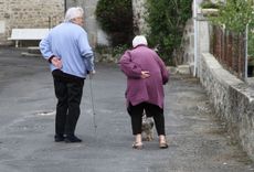 Twee ouderen staan op straat met een hand op hun onderrug. Een van hen gebruikt een wandelstok.