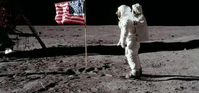 Een astronaut staat op het maanoppervlak naast een Amerikaanse vlag.