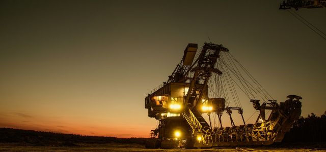 Een grote graafmachine met brandende lichten in een open mijn bij zonsondergang.