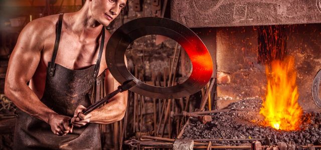 Smid met een leren schort houdt een gloeiende metalen ring vast naast een fel vuur.