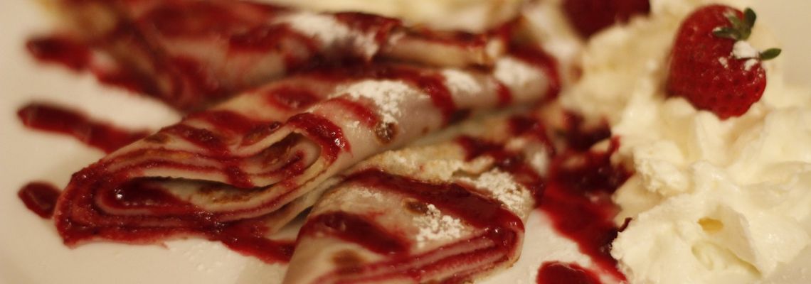 Gevouwen pannenkoeken met rode vruchtensaus, poedersuiker, slagroom en een aardbei.