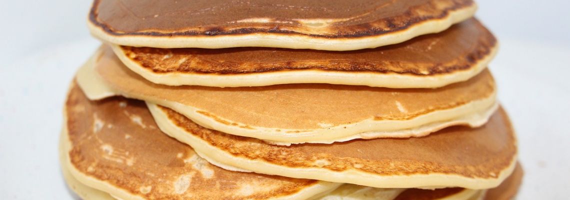 Een stapel dikke, goudbruine pannenkoeken op een wit bord.