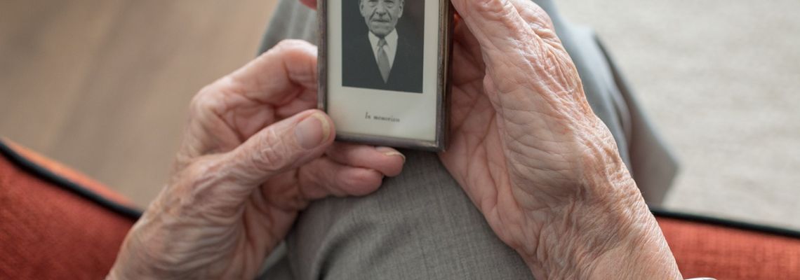 Gerimpelde handen houden een klein portret van een man vast.