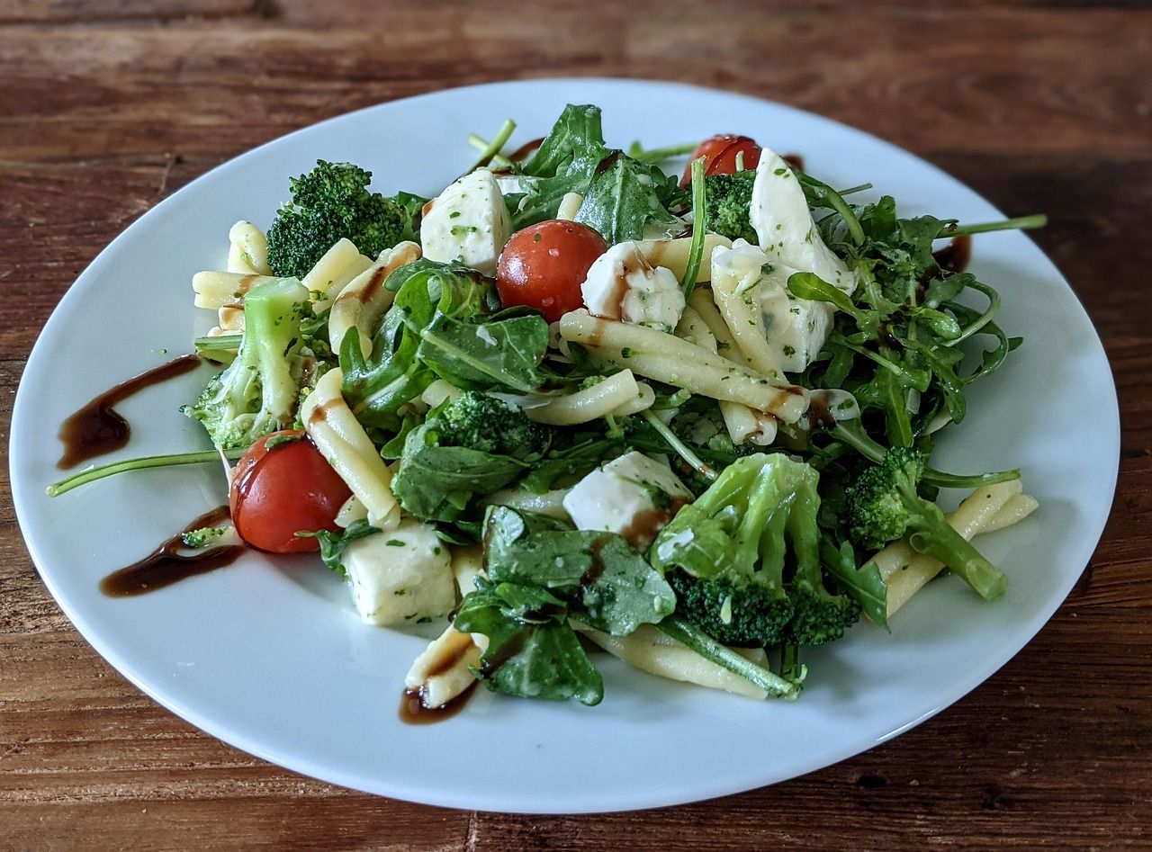 Een bord pastasalade met broccoli, kerstomaten, bladgroenten en witte kaas.