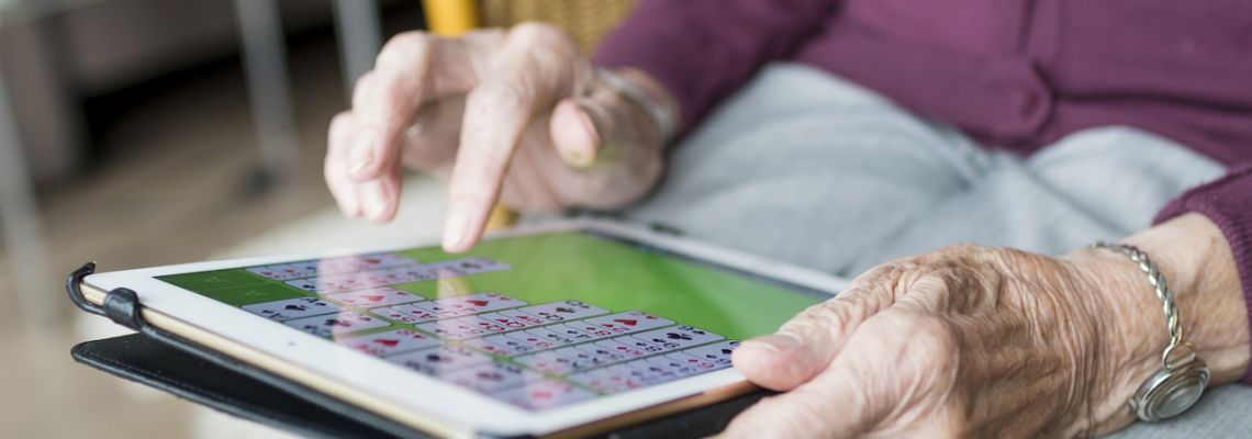 Een oudere persoon raakt met een vinger het scherm van een tablet aan.